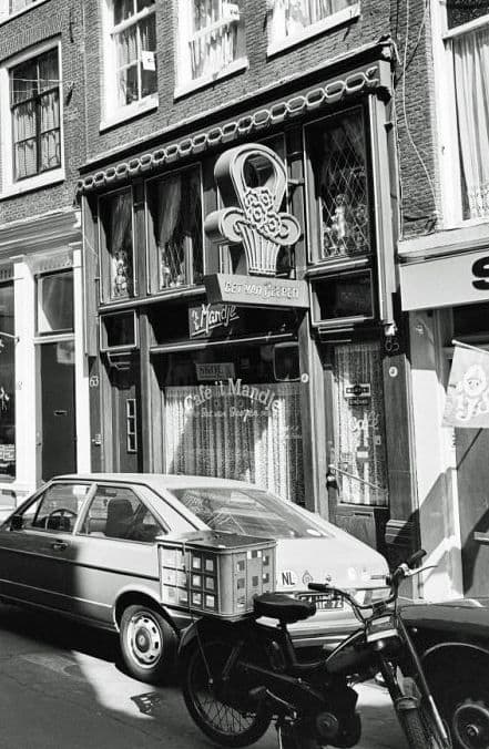 Zwart-witfoto van de gevel van café ’t Mandje op de Zeedijk in 1976, met een brommer en een auto voor de deur